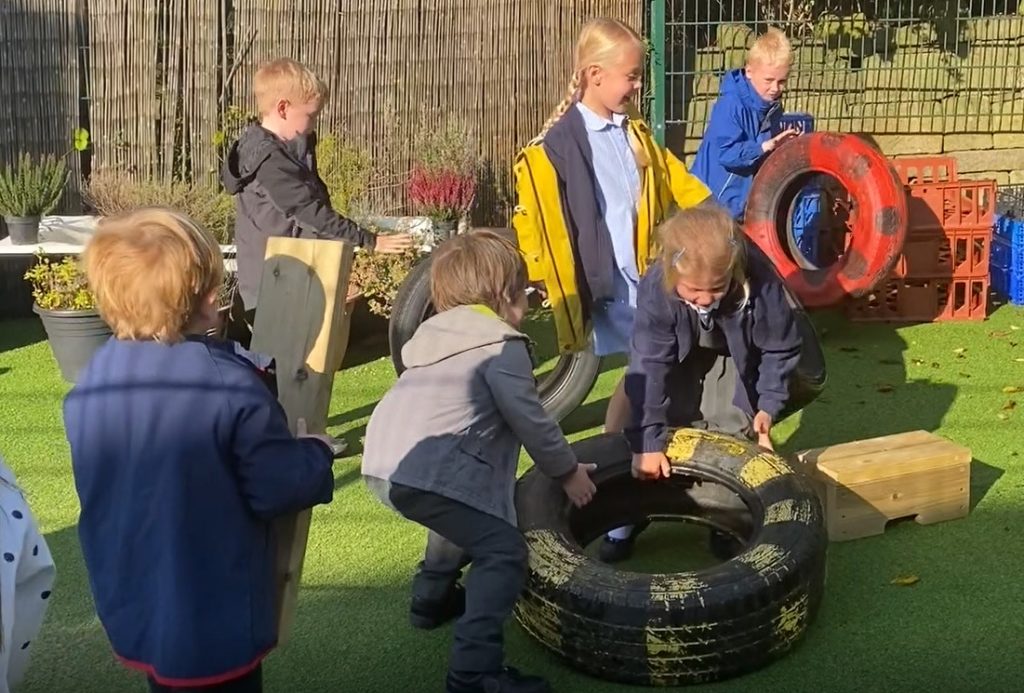 Children work together to lift and move tires and planks.