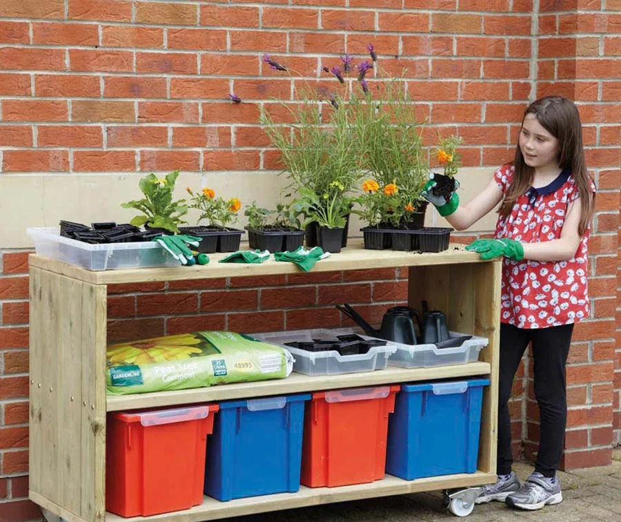 Image shows a Small Outdoor Mobile Storage Shelving Unit, containing plants on top and gardening tools underneath. A child is tending to one of the plants on the top.