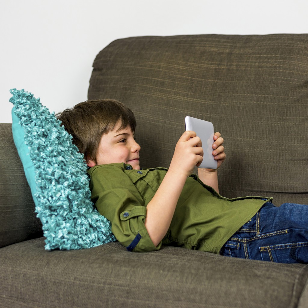 boy laying relaxed on sofa playing on his tablet