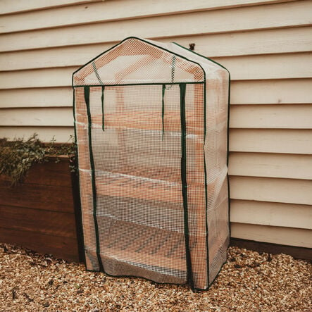 Image of an outdoor greenhouse with cover leaning against an outdoor wall.