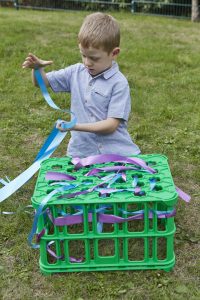 Loose parts play - a child threading material through the gaps in the creative crates