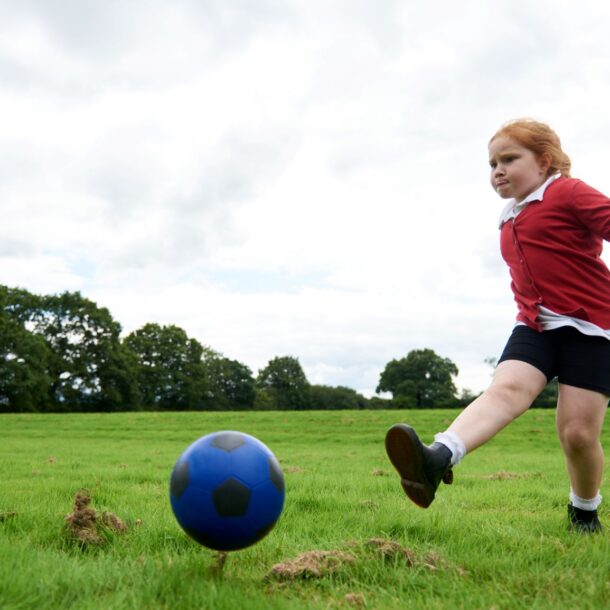 Young girl in red school uniform kicking a blue rubber football