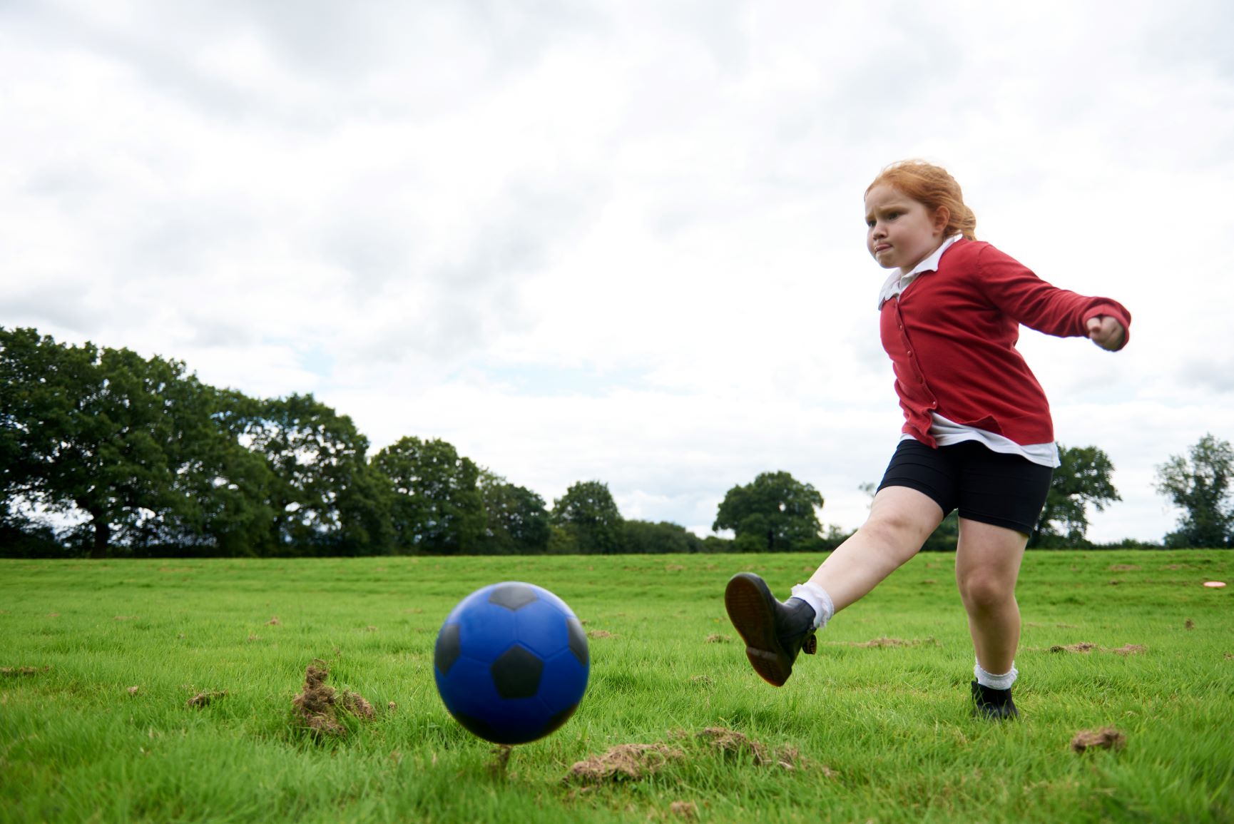 Young girl in red school uniform kicking a blue rubber football