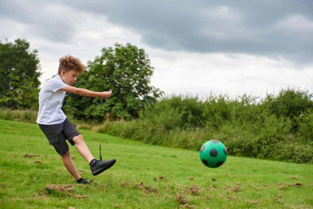 Young boy striking a green rubber football
