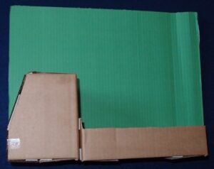 Cardboard cabin placed on top of a piece of green coloured corrugated card.