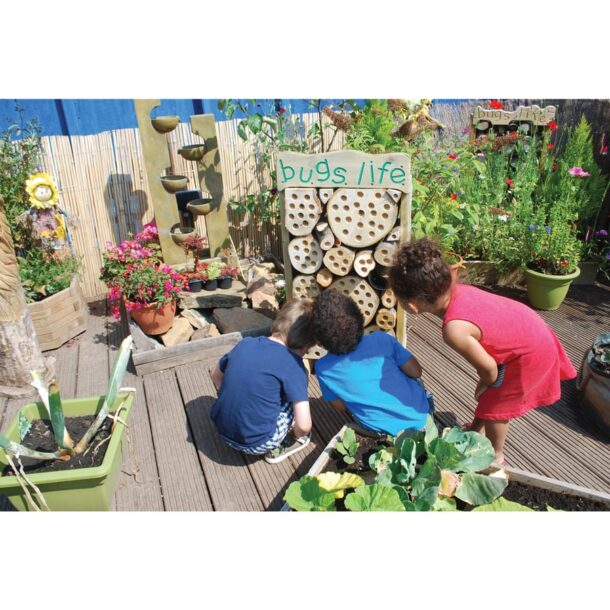 Image shows a giant outdoor bug hotel in a garden with three children looking into it.